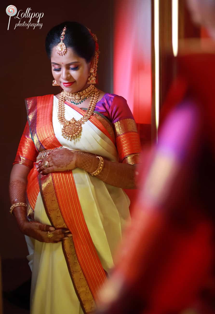 Expectant mother in a reflective pose, showcasing her ornate jewelry and henna-decorated hands, at her baby shower event in Chennai, by Lollipop Photography.