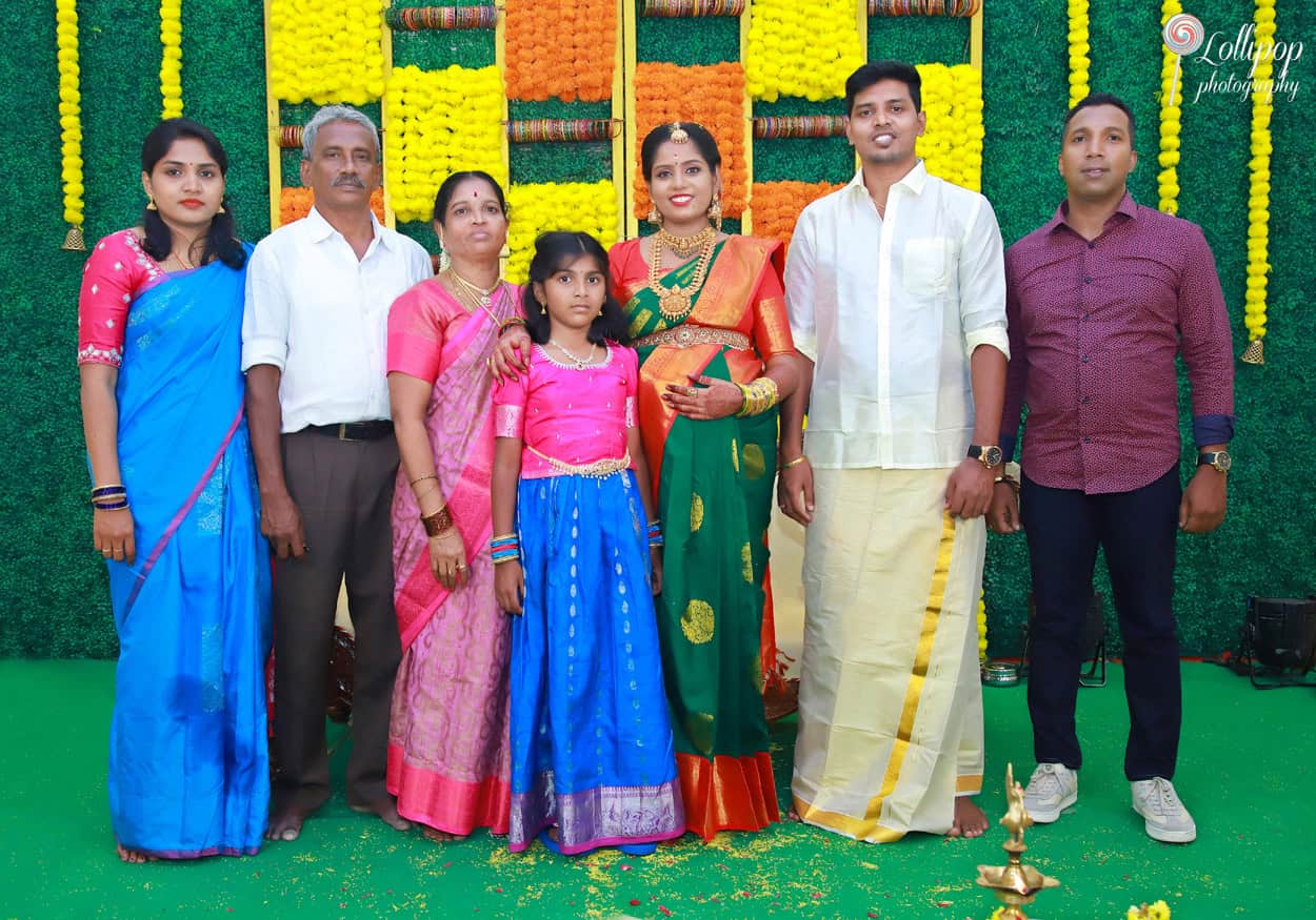 A cheerful group photo of an extended family celebrating a maternity occasion with a backdrop of bright marigolds in Chennai.