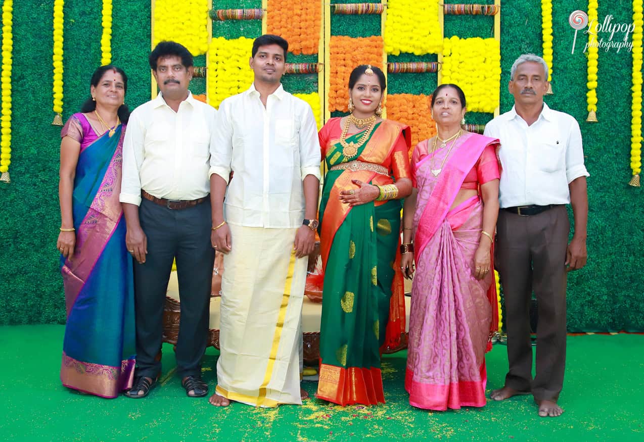 A grand family portrait during a maternity photoshoot in Chennai, showcasing smiles and traditional attire against a festive floral backdrop.