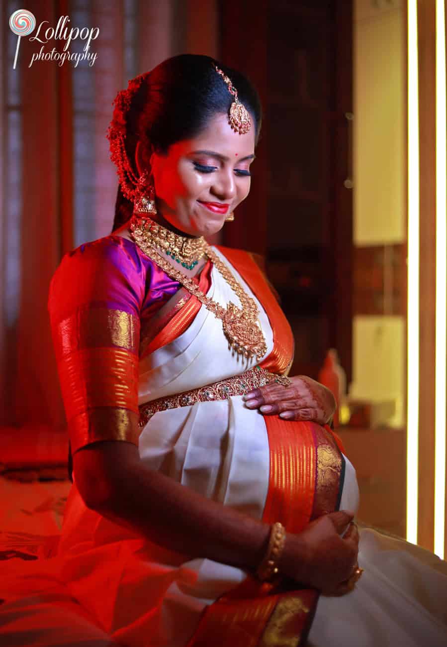 A radiant mother-to-be in traditional South Indian attire, standing by a warmly lit backdrop in Chennai.