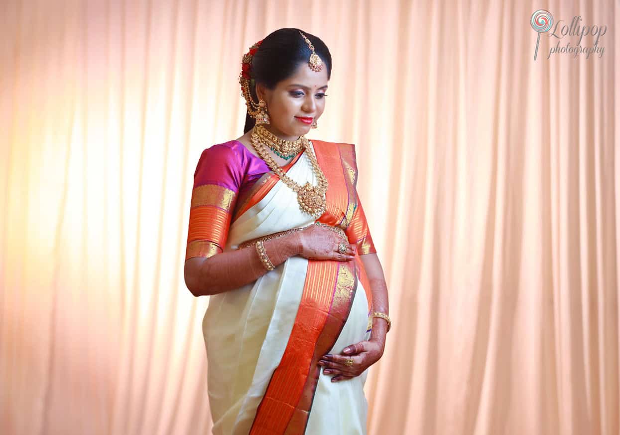 An elegant maternity portrait of a woman in a creamy saree complemented by golden borders, showcasing her pregnancy with grace in Chennai.