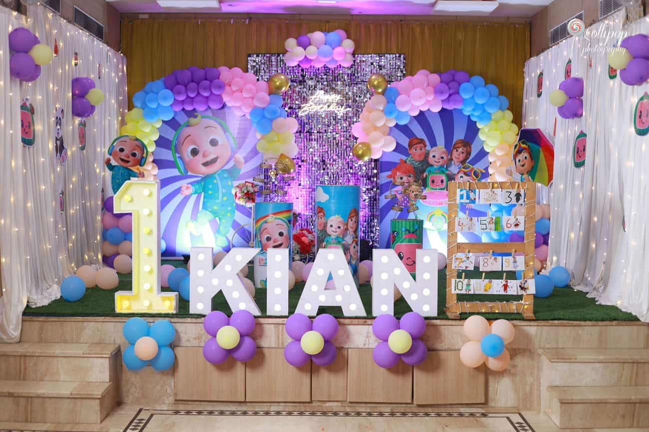 Vibrant birthday decoration for Kian's first birthday in Chennai, featuring colorful balloon arrangements, large illuminated letters spelling 'KIAN,' and cartoon character cutouts in a joyful celebration setup