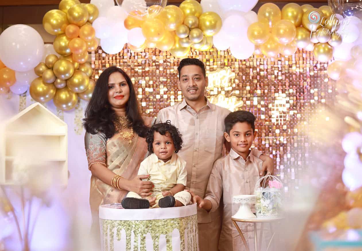 An elegant family portrait set against a golden-themed backdrop, celebrating Aryan’s birthday with smiles, captured by Lollipop Photography