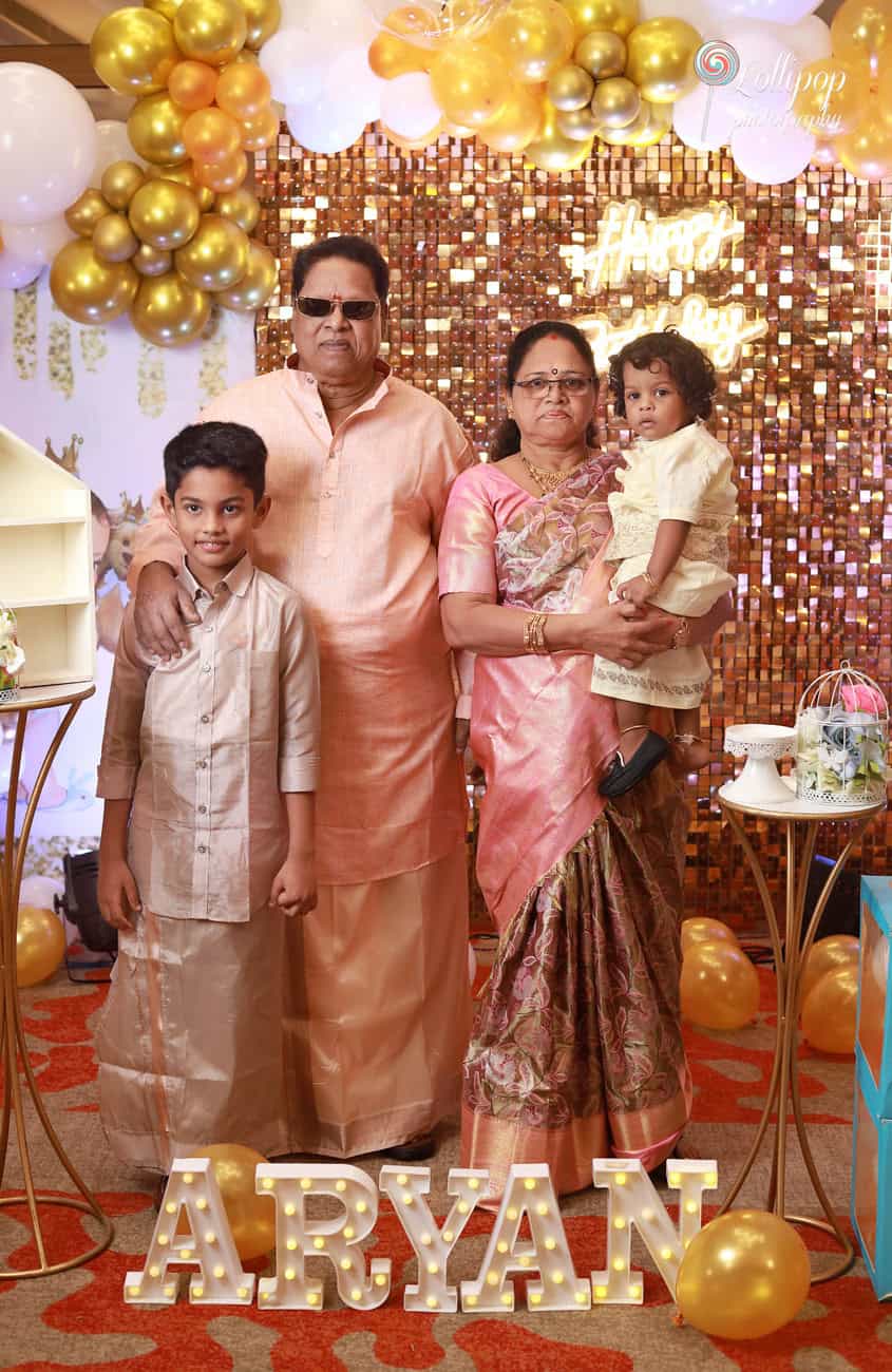 Aryan's grandparents pose with him and his sibling, celebrating amidst a golden-themed birthday decor, captured by Lollipop Photography