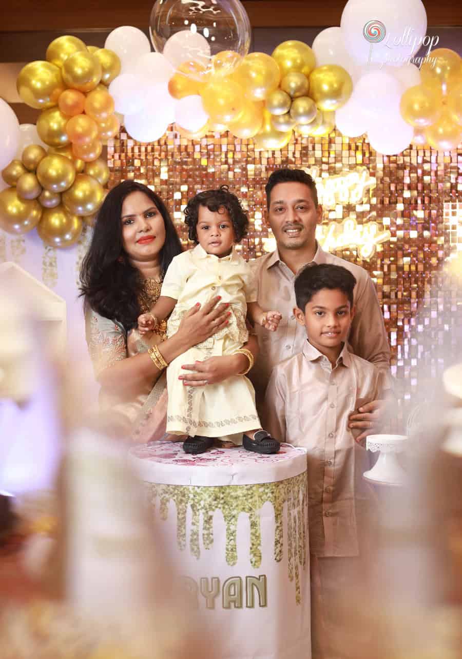 A joyful family photo in front of stunning gold decor, taken during Aryan’s birthday celebration, photographed by Lollipop Photography