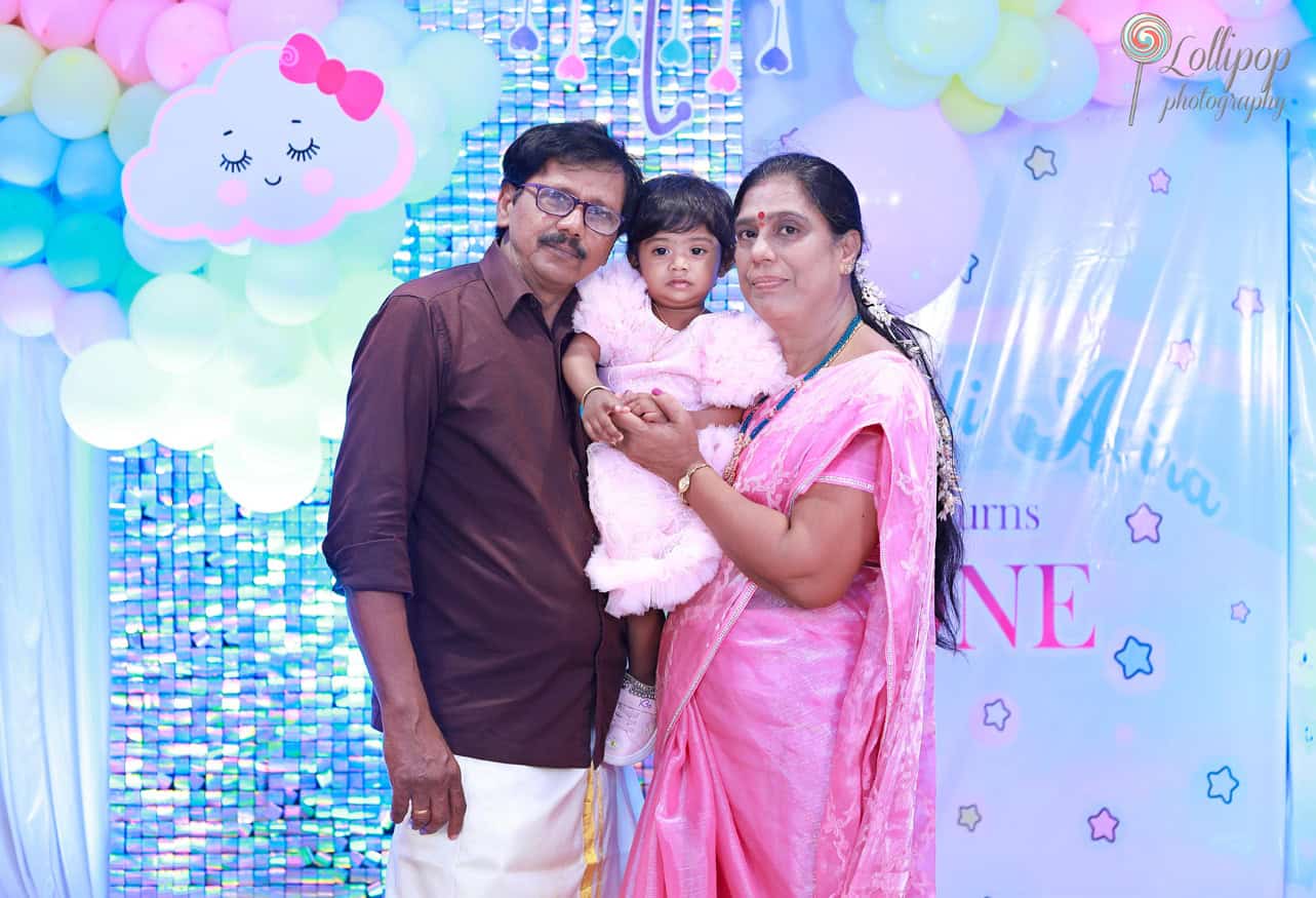 Kanali's grandparents proudly pose with her, dressed in a fluffy pink birthday dress, capturing a joyful family moment at the birthday celebration by Lollipop Photography.