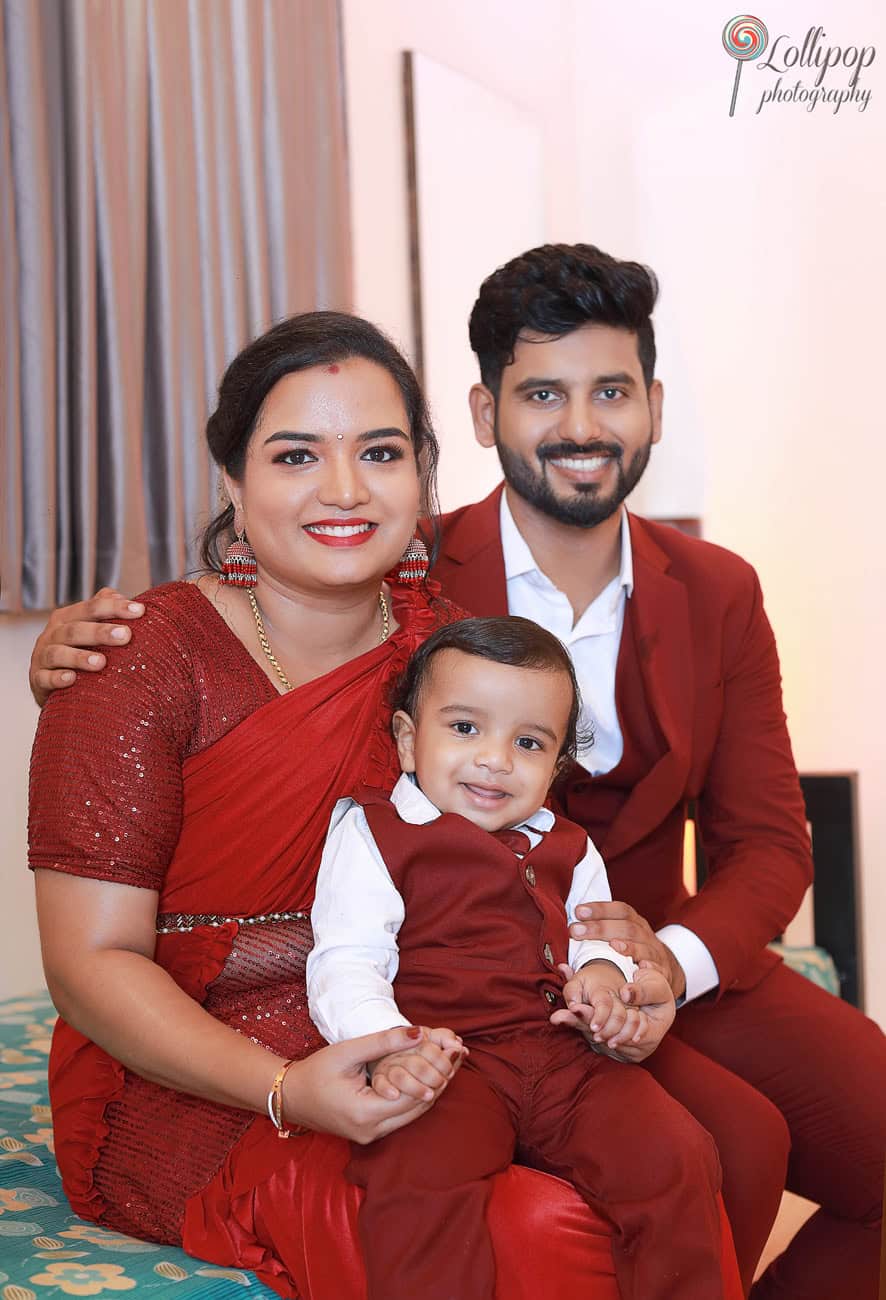 Kian with his parents, all dressed in matching red outfits, sharing a joyful moment at his first birthday celebration