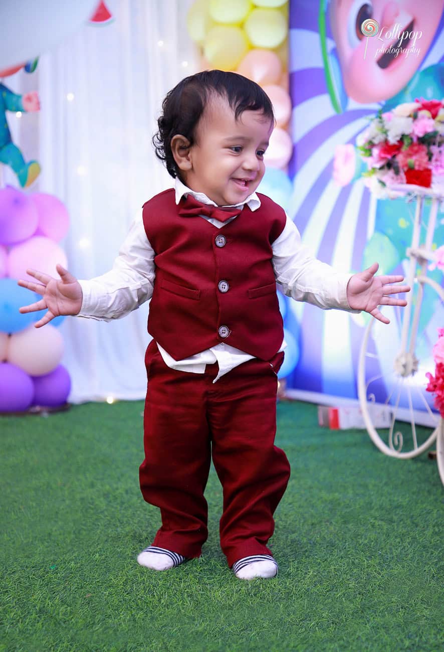 Happy little Kian walking and smiling at his birthday party surrounded by colorful decor, captured by Lollipop Photography in Chennai