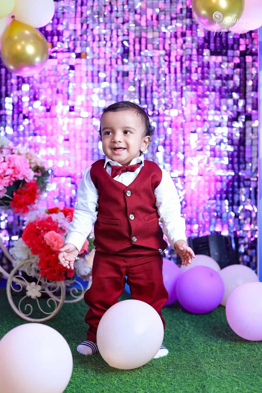 Cheerful Kian standing among pastel balloons, enjoying his first birthday celebration photoshoot in Chennai, courtesy of Lollipop Photography.