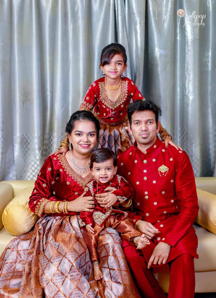 A heartwarming family portrait of Nathaniel with his parents and sister, dressed in elegant red and gold attire, captured by Lollipop Photography