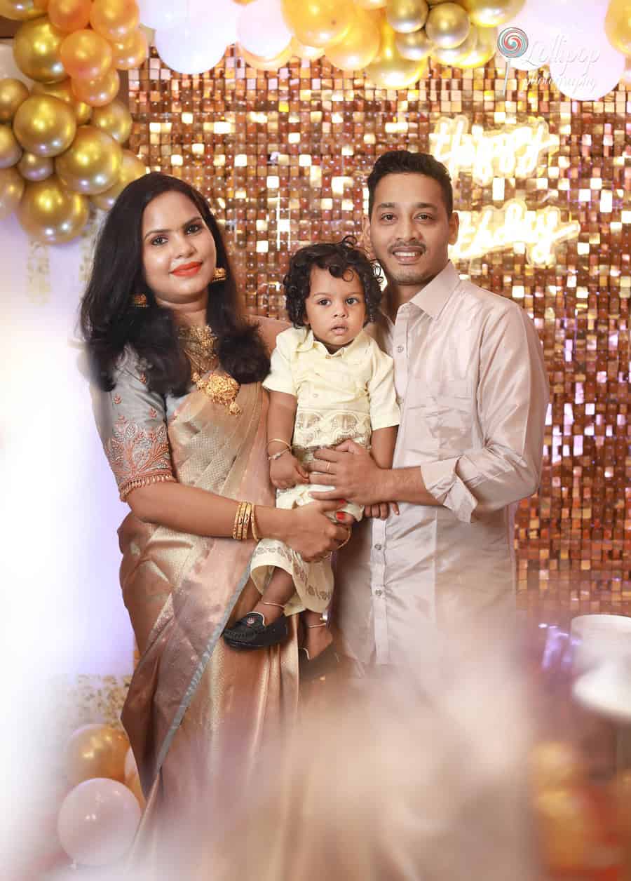 Aryan's parents hold him close in front of a golden birthday-themed backdrop, captured by Lollipop Photography