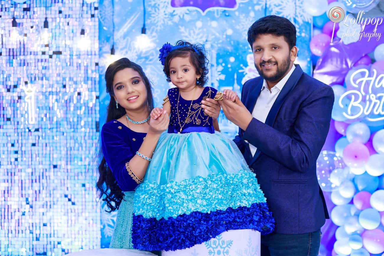 Pranika, dressed in a lovely blue and turquoise gown, with her smiling parents during her birthday celebration, captured by Lollipop Photography