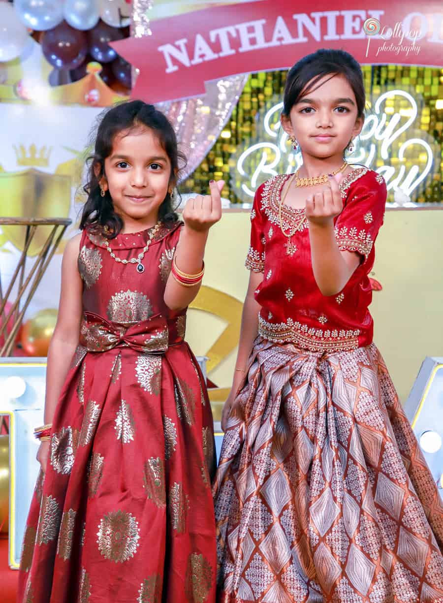 Two young girls dressed in festive attire celebrate Nathaniel’s birthday with big smiles and playful gestures