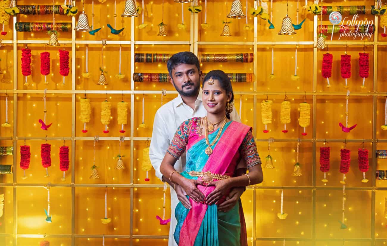 Arthi and Naveen Kumar posing in front of a beautifully decorated baby shower backdrop in Chennai, captured by Lollipop Photography