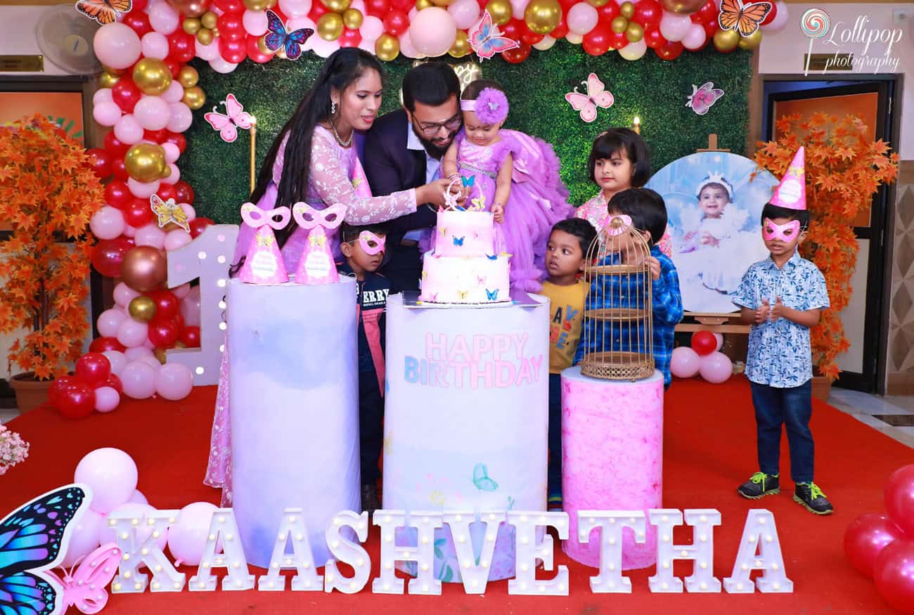 A joyful moment as the baby girl cuts her birthday cake with family and friends at her butterfly-themed birthday party. Captured by Lollipop Photography, Chennai.