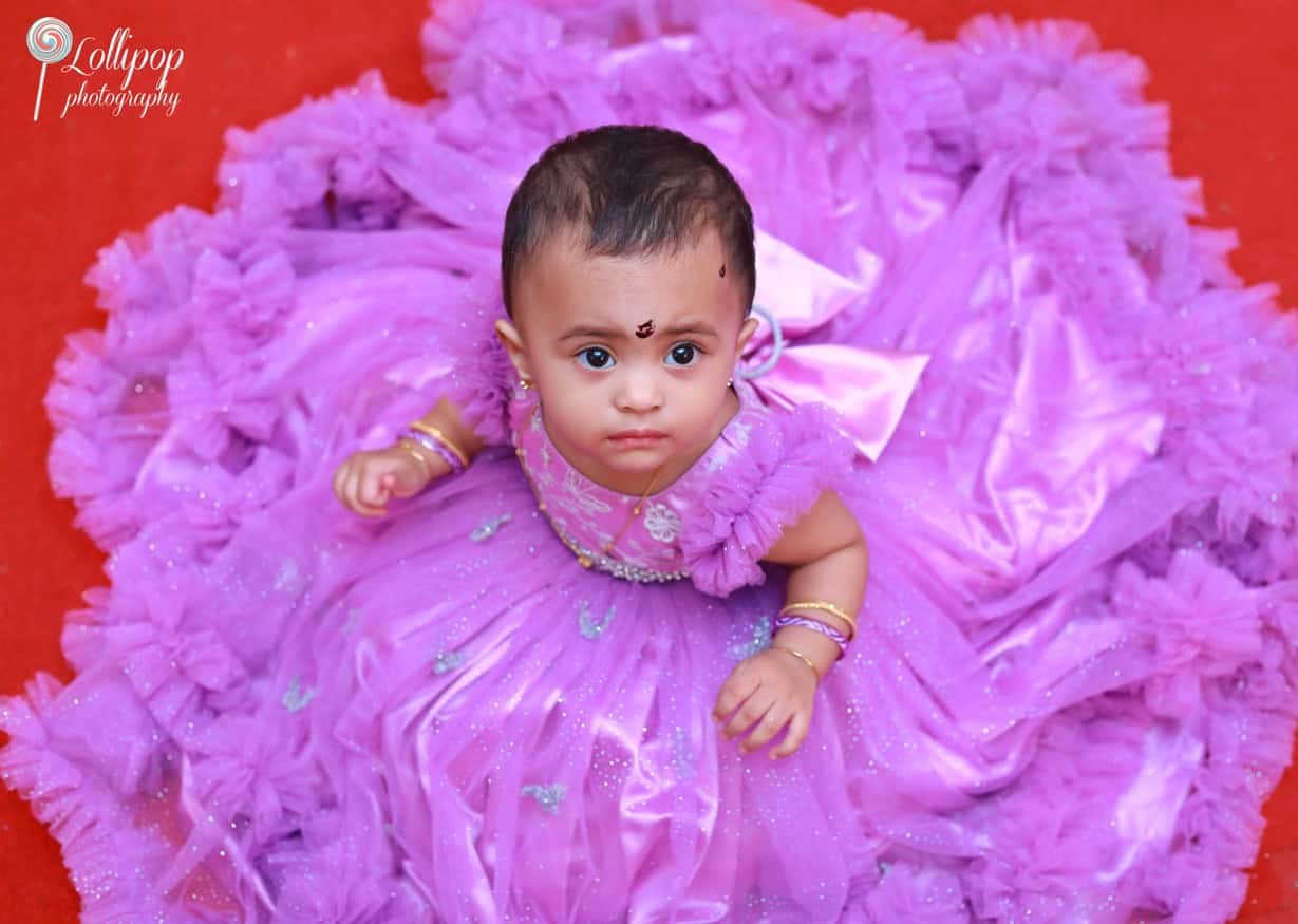 Close-up of a baby girl in a lavender gown looking up at the camera, surrounded by her beautiful birthday dress. Captured by Lollipop Photography, Chennai