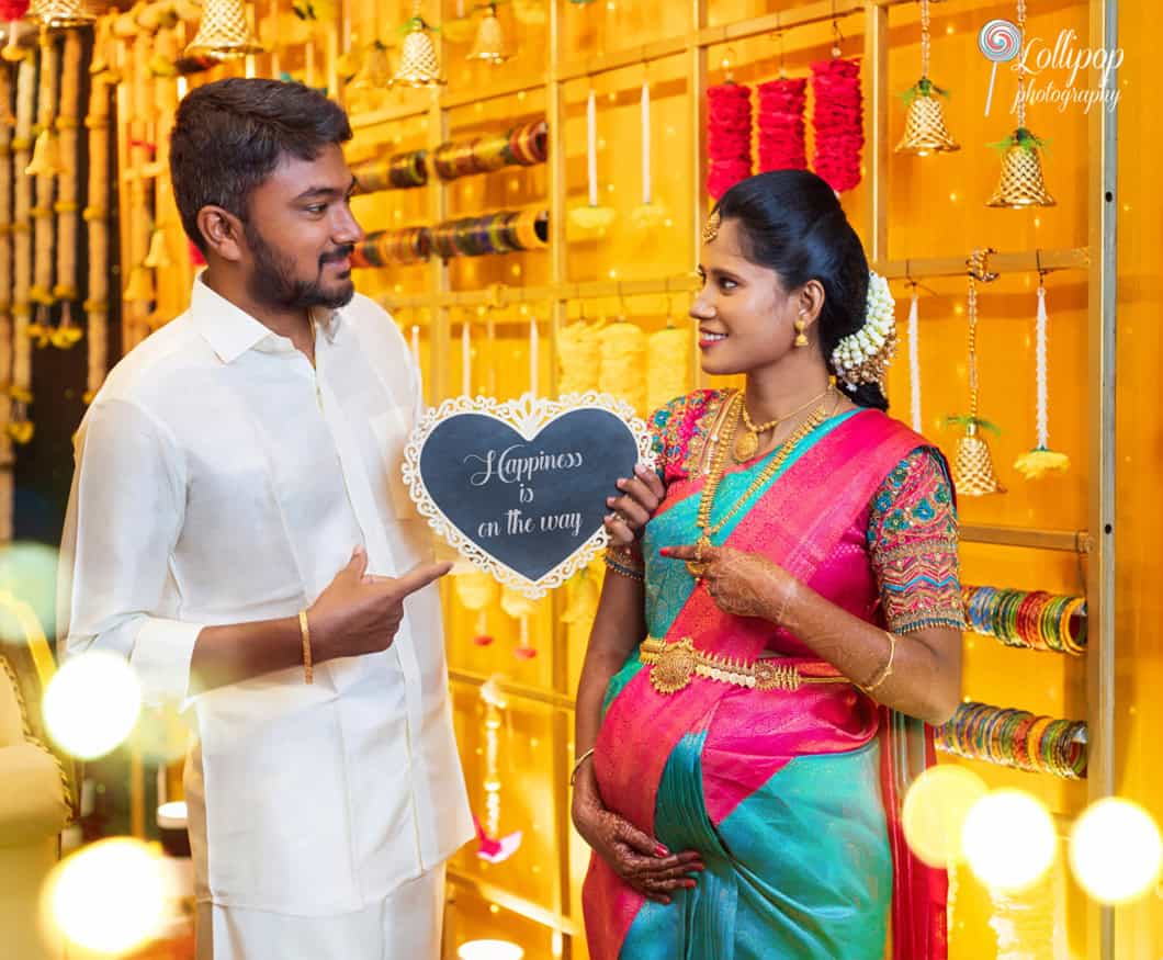 Charming baby shower photoshoot in Chennai, with the couple holding a sign reading 'Happiness is on the way,' captured by Lollipop Photography.