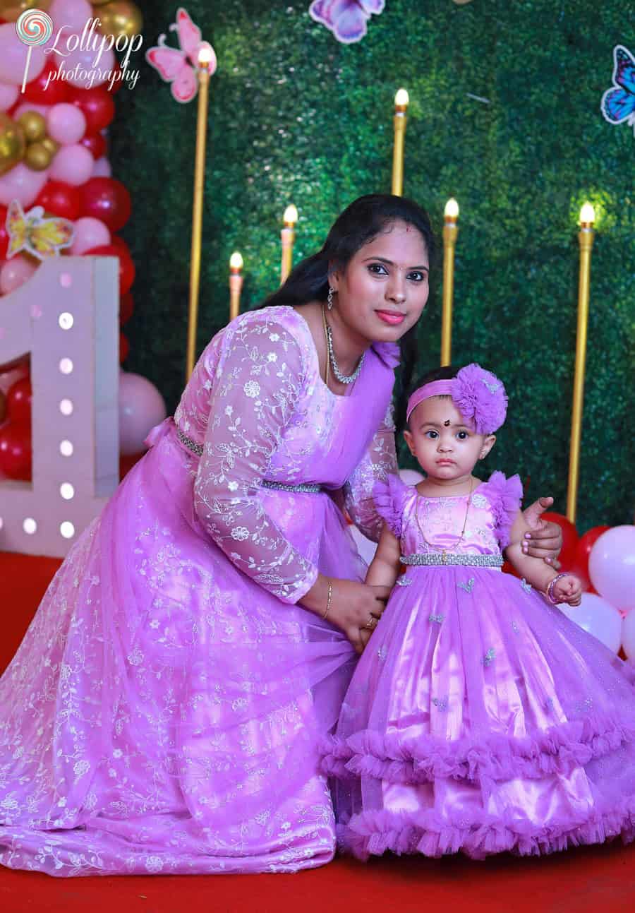 A mother and daughter duo in matching purple dresses, posing at a butterfly-themed birthday setup. Birthday photoshoot by Lollipop Photography, Chennai.