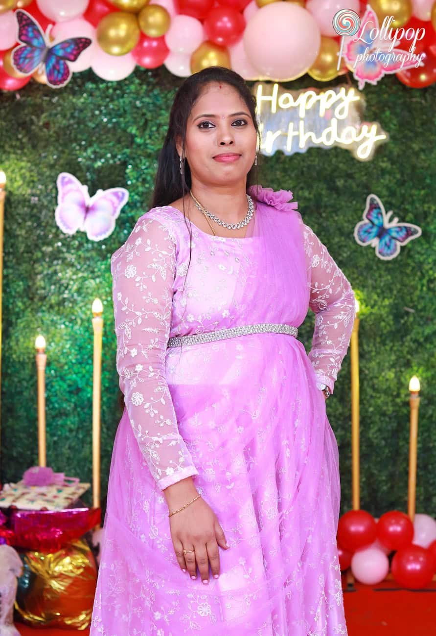 Mother in a beautiful purple dress standing in front of a butterfly-themed birthday backdrop. Birthday photoshoot by Lollipop Photography, Chennai