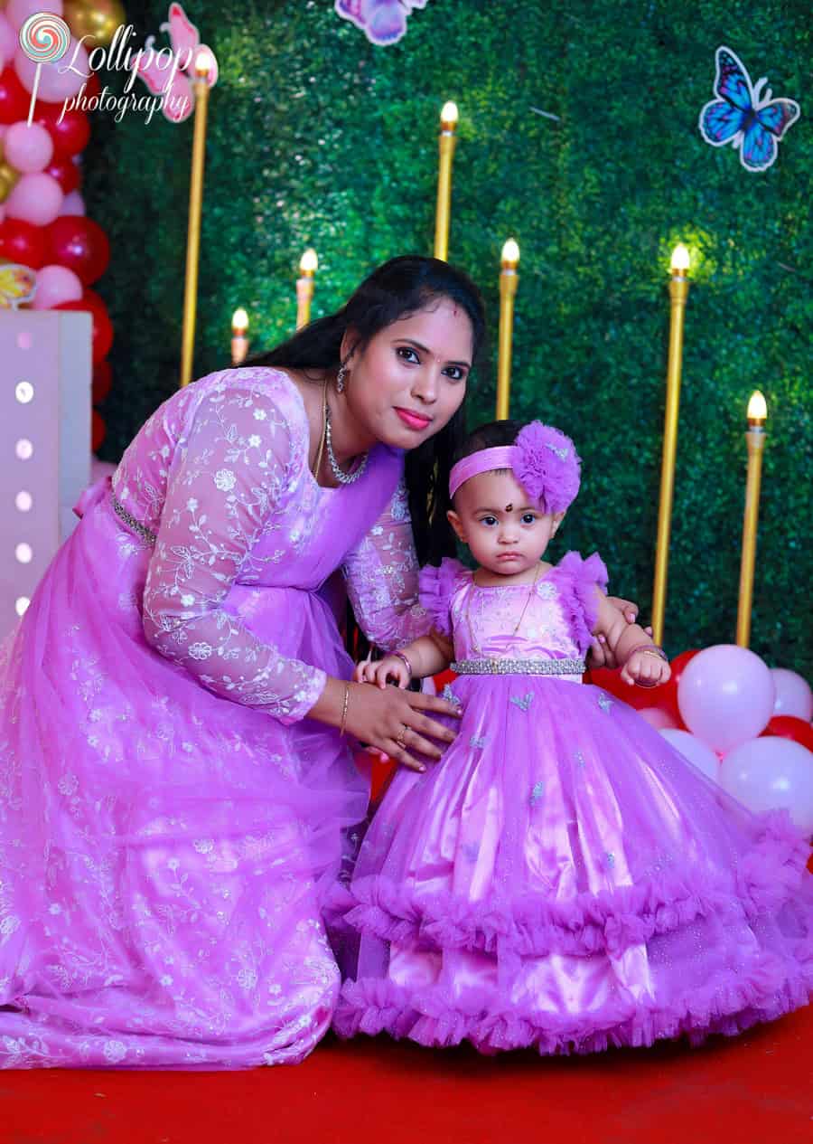 A mother and her baby girl in matching lavender dresses at a vibrant butterfly-themed birthday setup. Captured by Lollipop Photography, Chennai