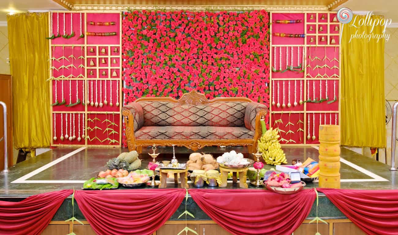 Elegant stage decorated with vibrant red floral backdrop and traditional arrangements for Aswini Naresh’s baby shower in Chennai, photographed by Lollipop Photography