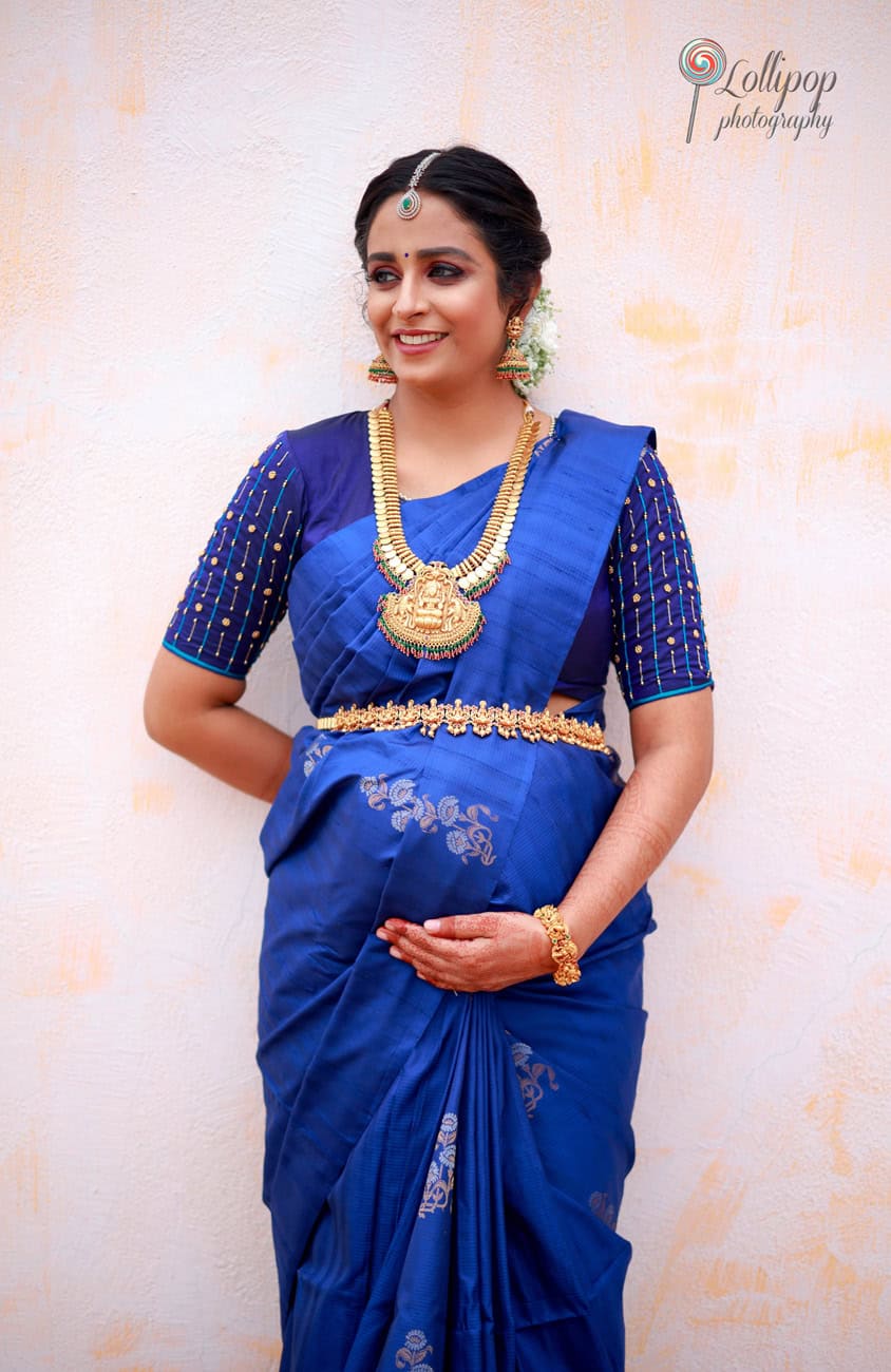 An elegant full-length portrait of a pregnant mother in a vibrant blue saree with gold accents, standing gracefully during her baby shower photoshoot by Lollipop Photography in Chennai