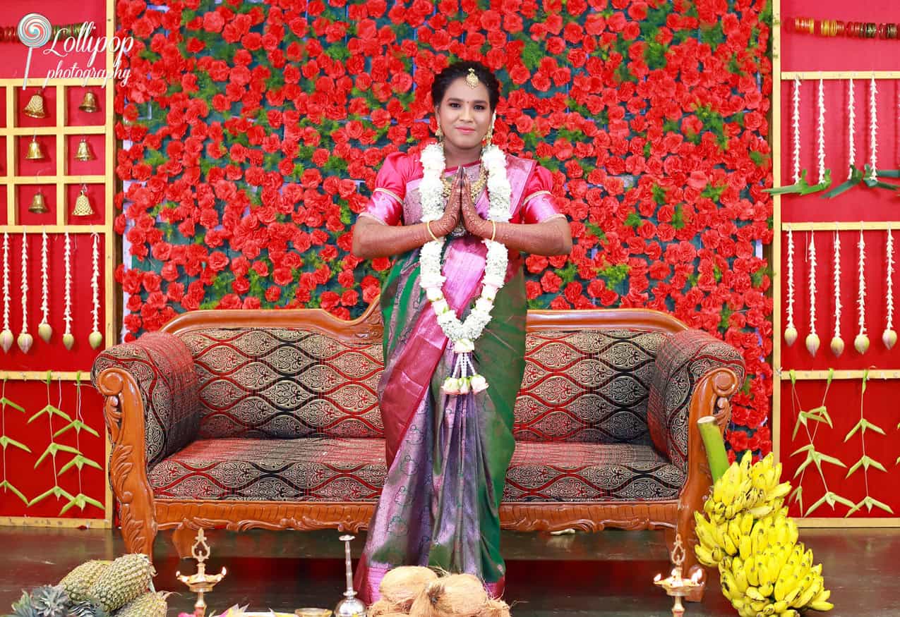 An expecting mother, dressed in a colorful saree, greets with folded hands in a traditional setup filled with ceremonial decorations, photographed by Lollipop Photography in Chennai