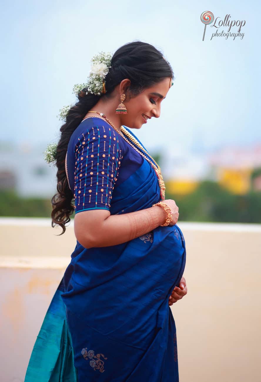 A joyful mom-to-be in traditional blue attire, lovingly gazing down at her baby bump during her baby shower photoshoot in Coimbatore by Lollipop Photography