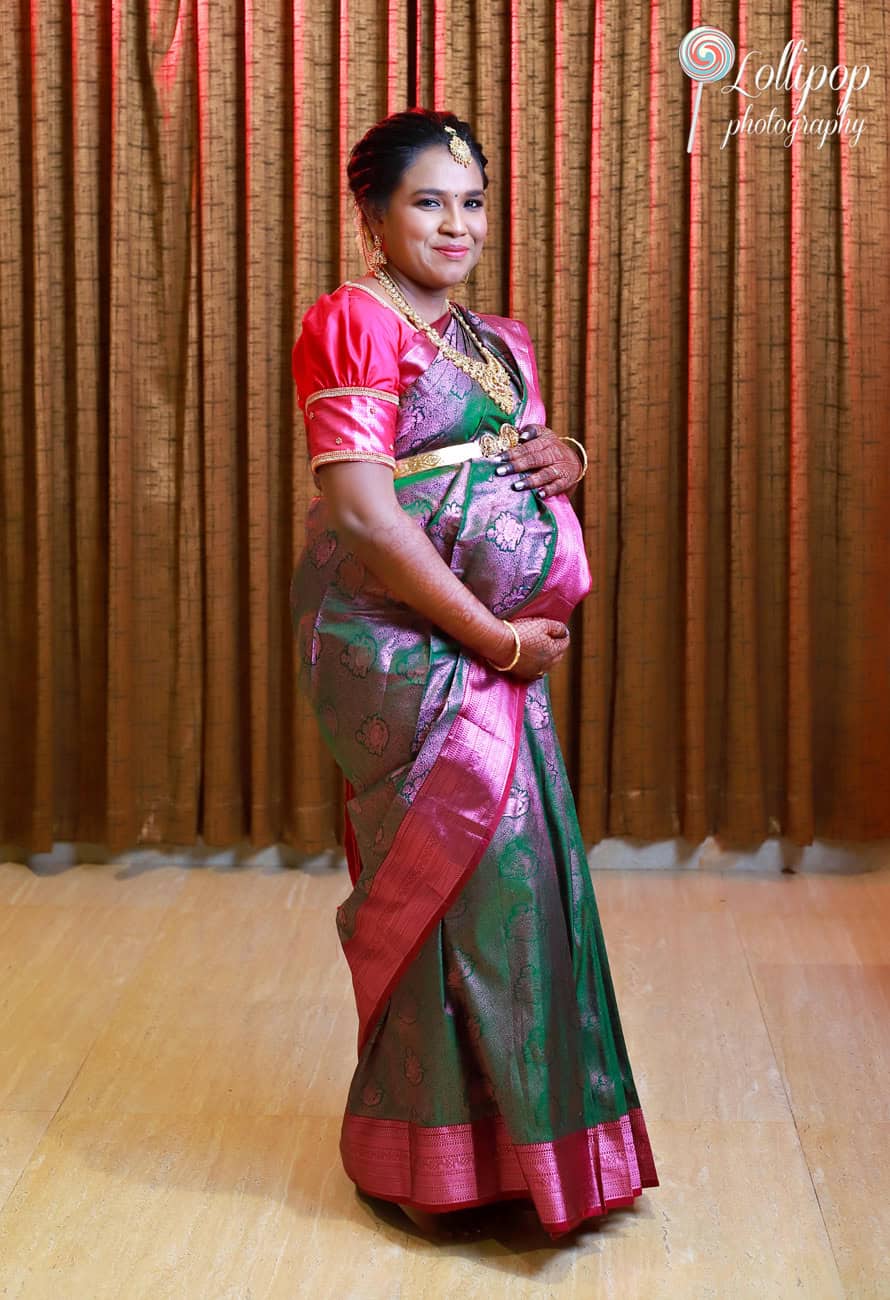 A mother-to-be in a bright saree stands gracefully with a smile, highlighting her joy in this maternity portrait by Lollipop Photography