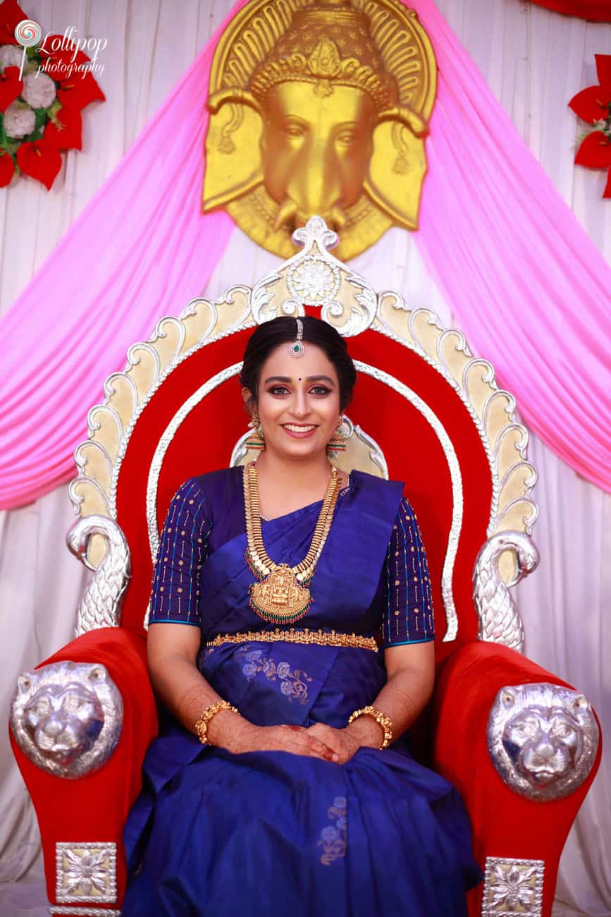 Pavithra, dressed in a blue saree, sits elegantly on a throne chair as part of her baby shower celebration, bringing out the essence of tradition and grace in Coimbatore.