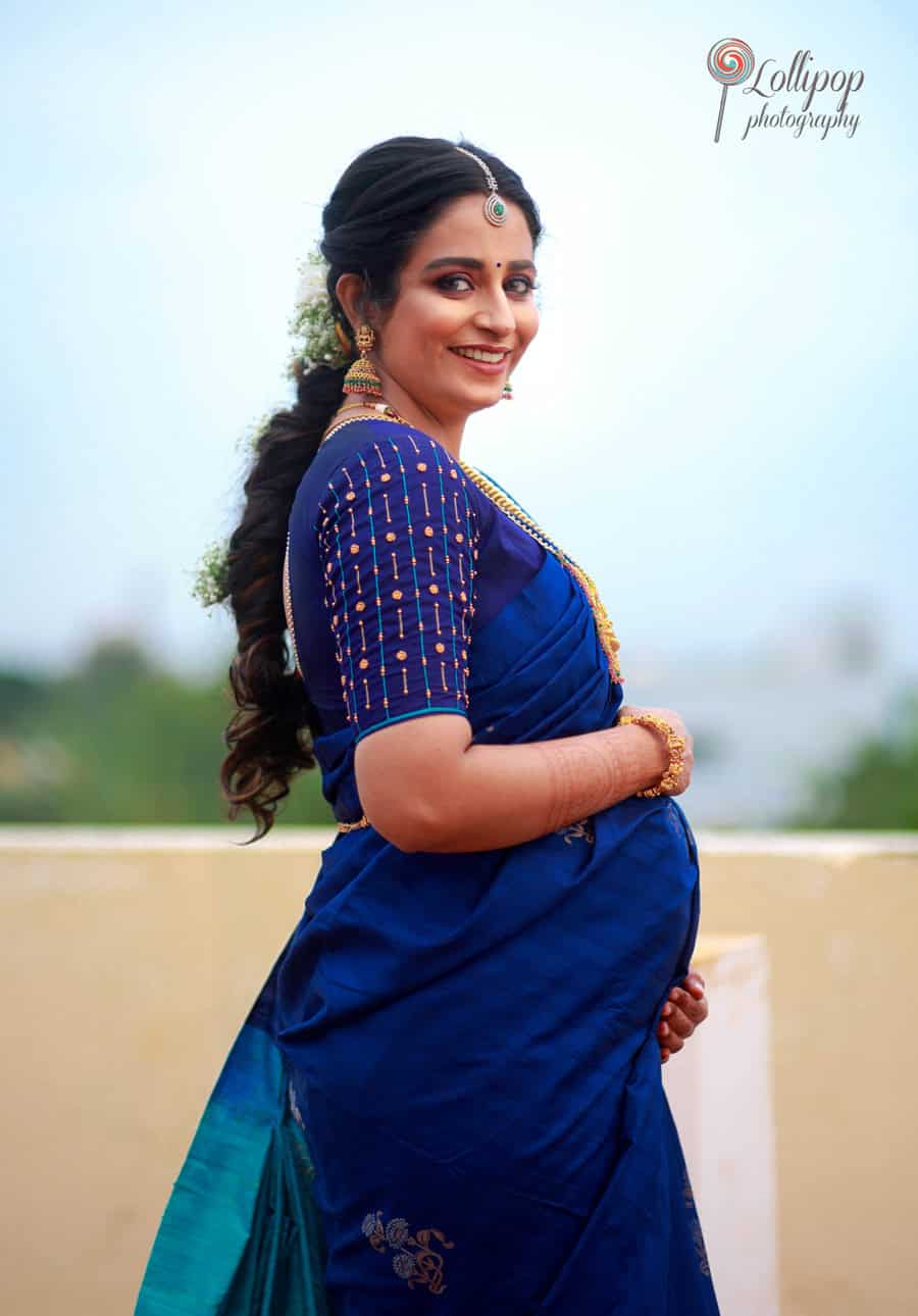 A radiant mom-to-be dressed in a blue saree, captured smiling gracefully during her baby shower photoshoot in Coimbatore by Lollipop Photography