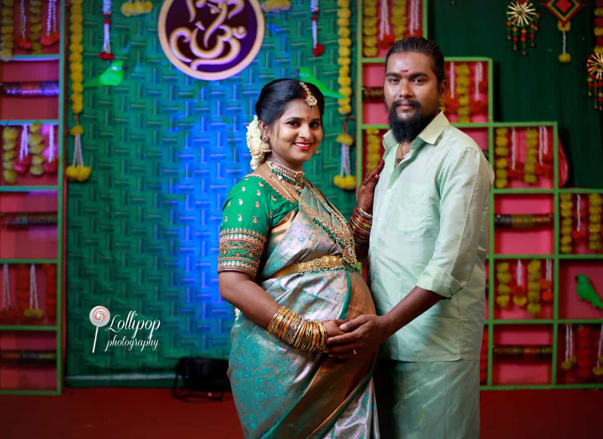 Sharmila, dressed in green and gold, poses with her husband against a stunning backdrop during her baby shower celebration in Coimbatore, photographed by Lollipop Photography.