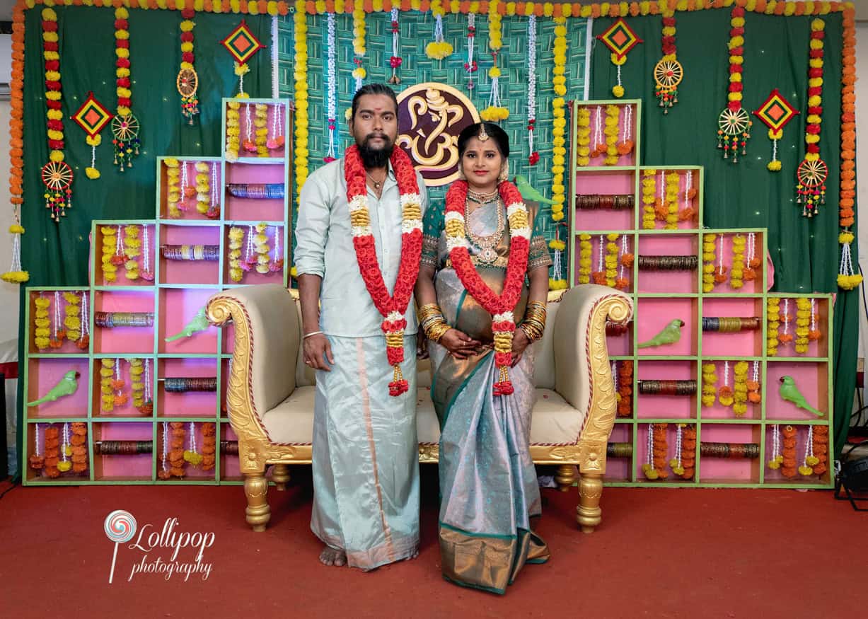 Sharmila and her husband stand together on the beautifully decorated baby shower stage, adorned in traditional attire with vibrant floral garlands, captured by Lollipop Photography in Coimbatore.