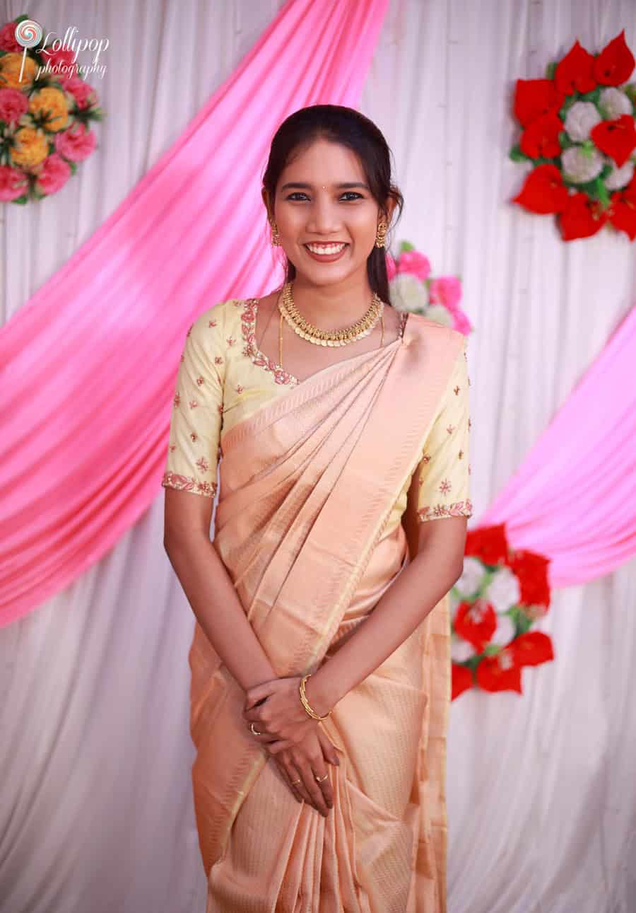 A young woman in a beige saree smiles joyfully at Pavithra's baby shower in Coimbatore, adding to the cheerful and vibrant atmosphere